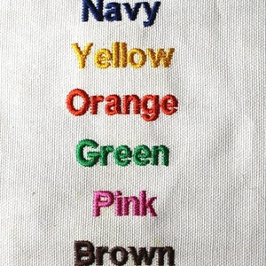 Puede incluir: Una muestra de tela blanca con nombres de colores bordados en diferentes colores. Los colores son: negro, turquesa, rojo, azul marino, amarillo, naranja, verde, rosa, marr&oacute;n, morado y verde lima.
