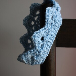 May include: A light blue crocheted headband with a scalloped edge. The headband is draped over a wooden chair.