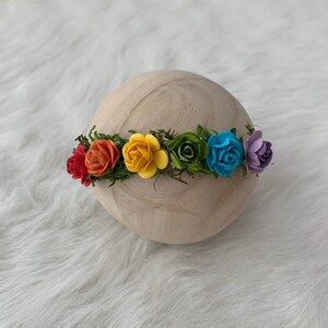 K&ouml;nnte beinhalten: Eine Regenbogen-Blumenkrone mit roten, orangen, gelben, gr&uuml;nen, blauen und violetten Bl&uuml;ten. Die Krone besteht aus Filzblumen und gr&uuml;nen Bl&auml;ttern.