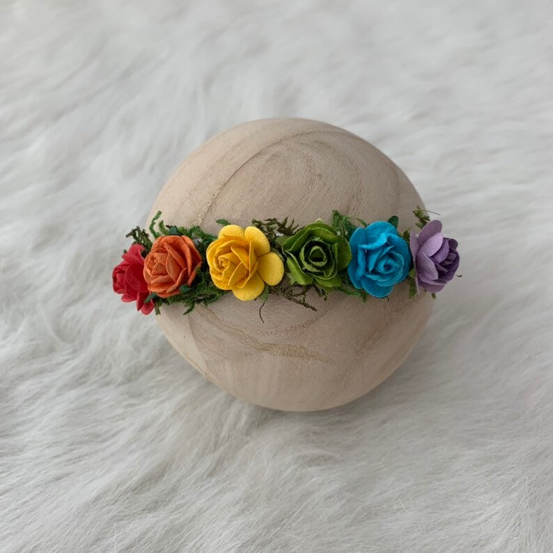 K&ouml;nnte beinhalten: Eine Regenbogen-Blumenkrone mit roten, orangen, gelben, gr&uuml;nen, blauen und violetten Bl&uuml;ten. Die Krone besteht aus Filzblumen und gr&uuml;nen Bl&auml;ttern.