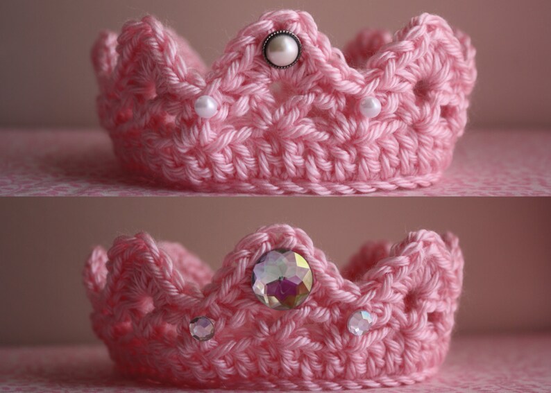 May include: Two pink crocheted crowns with decorative embellishments. The top crown has white pearl-like beads and a larger pearl-like bead in the center. The bottom crown has iridescent rhinestones.