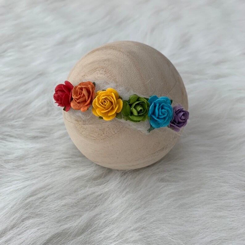K&ouml;nnte beinhalten: Eine Regenbogen-Blumenkrone mit roten, orangen, gelben, gr&uuml;nen, blauen und violetten Bl&uuml;ten. Die Krone ist aus Filz und perfekt f&uuml;r Neugeborenenfotografie.