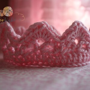 May include: A pink crocheted crown with a delicate openwork design. The crown is made with a soft yarn and has a delicate, feminine look.
