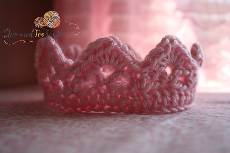 May include: A pink crocheted crown with a delicate openwork design. The crown is made with a soft yarn and has a delicate, feminine look.