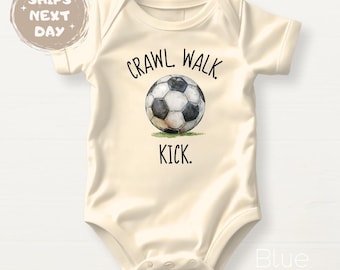 May include: Cream-colored baby bodysuit with the text "Crawl Walk Kick" surrounding a soccer ball graphic. The bodysuit is short-sleeved and has a snap closure at the bottom. The soccer ball is black and white.