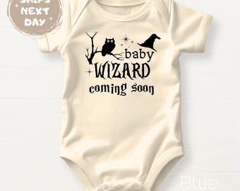 May include: Cream-colored baby onesie with a black graphic featuring an owl perched on a branch, a wizard hat, and the words "baby WIZARD coming soon." The onesie is short-sleeved.