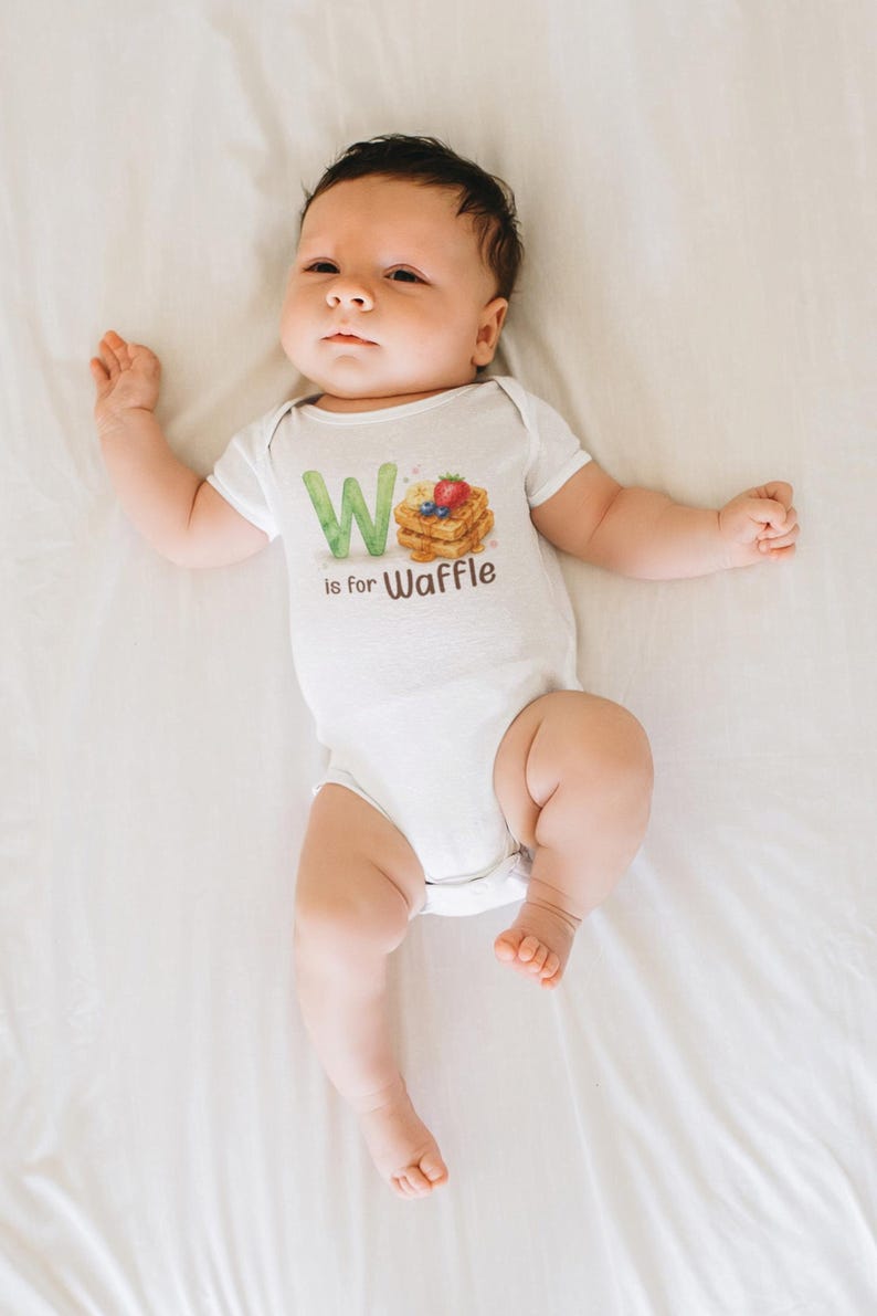 May include: A white baby onesie with the text "W is for Waffle" and a watercolor illustration of waffles, blueberries, and a strawberry. The baby is lying on a white sheet.