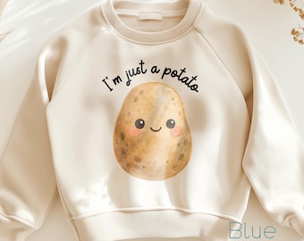 May include: Cream-colored sweatshirt featuring a smiling potato graphic with the text "I'm just a potato." The potato has rosy cheeks and a happy expression. The sweatshirt has a ribbed neckline, cuffs, and hem.