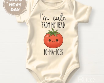 May include: Cream-colored baby onesie with the text "I'm cute FROM MY HEAD TO-MA-TOES" and a cartoon tomato illustration. The tomato is red with a green stem and smiling face. The onesie is a short-sleeved style.