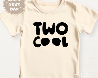 May include: Cream-colored toddler t-shirt with the words "TWO COOL" in bold black letters. The "O" in "COOL" is replaced with a pair of sunglasses. A round sticker that says "SHIPS NEXT DAY" is in the upper left corner.