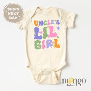 May include: A white baby onesie with short sleeves and a colorful graphic that says "Uncle's Lil' Girl" with flowers and hearts.