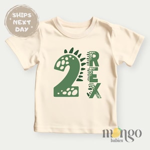 May include: A cream coloured short-sleeved t-shirt with a green dinosaur graphic and the text "2 REX".