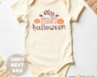 May include: Cream-colored baby bodysuit with the text "My First Halloween" in maroon. The design includes two orange pumpkins, spiders, and a spiderweb. The bodysuit has short sleeves and snap closures.