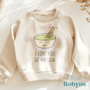 May include: A beige sweatshirt with a graphic of a green matcha bowl with a whisk and the text "I love you so matcha".