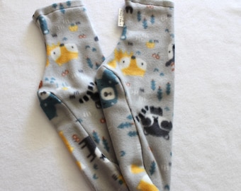 Puede incluir: Un par de calcetines de forro polar grises con un estampado repetido de zorros amarillos, osos azules y mapaches negros. Los calcetines también tienen pequeños árboles azules y círculos naranjas. Los calcetines están sobre una superficie blanca.
