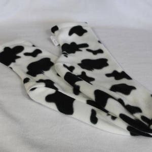 May include: A pair of cozy socks with a cow print design. The socks are white with large black spots, creating a playful and unique pattern. The socks are made of a soft material.