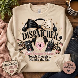 May include: A beige crewneck sweatshirt featuring a graphic of a large black and white bow, a headset, a smartphone displaying 911, a walkie-talkie, and a pink heart with 911. Text reads: DISPATCHER, Cute Enough to Care, Tough Enough to Handle the Call.