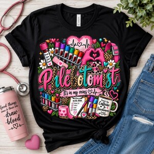 Puede incluir: Una camiseta negra con un gráfico colorido de tubos de ensayo, un corazón, un estetoscopio y el texto Phlebotomist It's in my veins. El diseño incluye una lista de verificación de extracción de sangre y una taza con Fueled by Caffeine & Vacutainers.