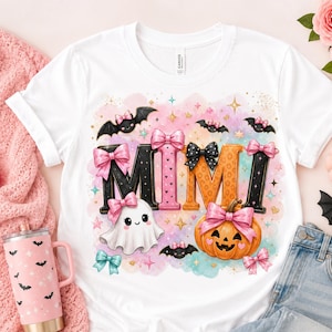 Puede incluir: Una camiseta blanca con la palabra MIMI en letras grandes y coloridas decoradas con patrones rosas, negros y naranjas. El diseño incluye un fantasma tierno, una calabaza, murciélagos pequeños y lazos rosas sobre un fondo de acuarela en tonos pastel.