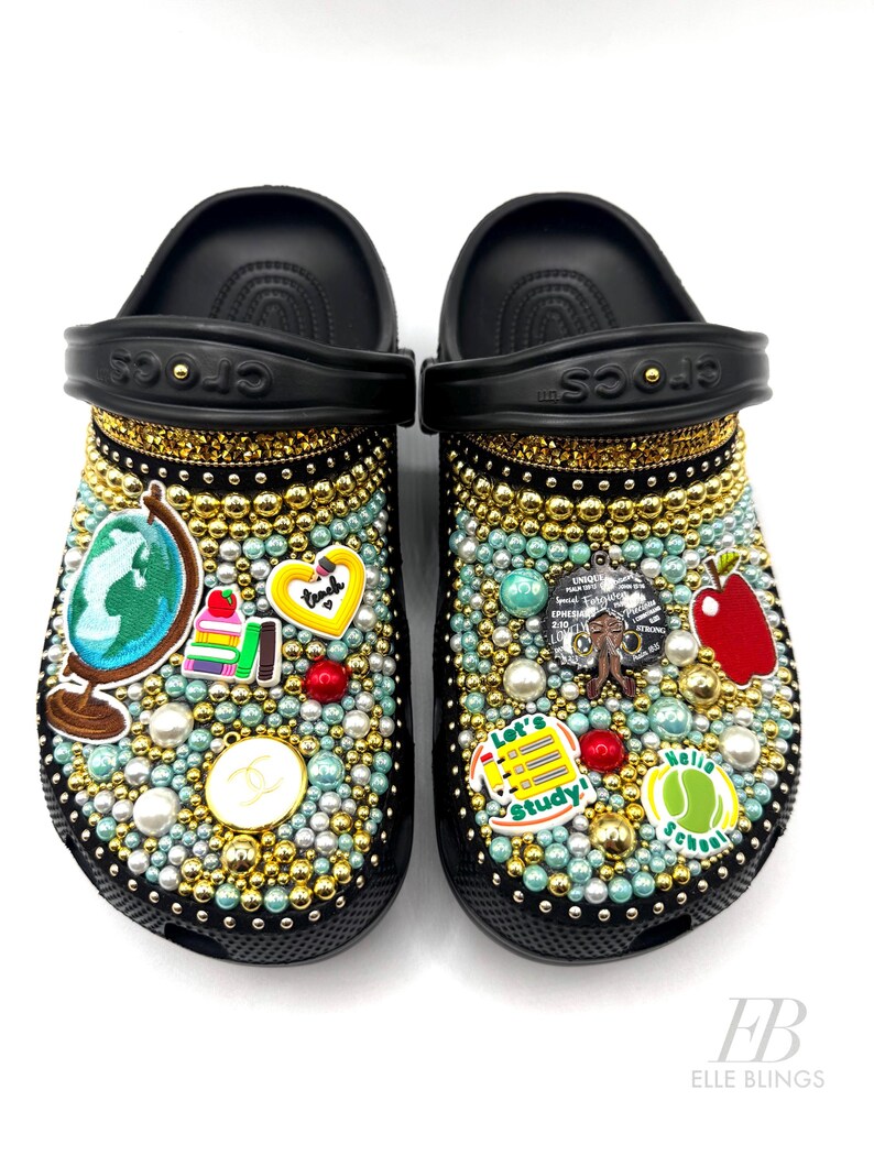 May include: Black and gold custom decorated clogs with a school theme. The clogs are covered in rhinestones, pearls, and charms. The charms include a globe, books, an apple, a heart, and a tennis ball. The text "Let's Study!" and "Hello School" are also included.