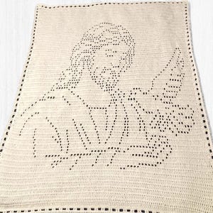 Puede incluir: Manta de ganchillo color crema con una imagen detallada de una persona con barba y una paloma. La imagen está creada con puntadas negras y la manta tiene un borde negro.