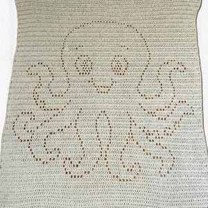 May include: A rectangular off-white crochet blanket featuring a central openwork design of an octopus. The octopus pattern is created using negative space within the dense crochet stitches, displaying a rounded head, two eyes, and eight tentacles.