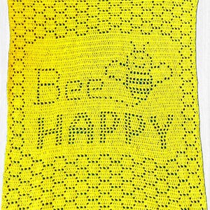 May include: A bright yellow rectangular crochet blanket featuring an openwork pattern that spells out the text Bee HAPPY. The design includes a stylized bee graphic integrated into the crochet stitches, surrounded by a decorative honeycomb border.