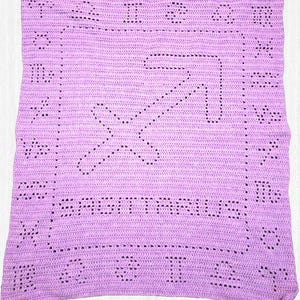 May include: A lavender crocheted blanket featuring the Sagittarius zodiac symbol in the center. The blanket has the word "SAGITTARIUS" and other zodiac symbols crocheted around the border. The blanket is made of soft yarn.