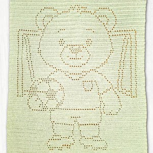 May include: A rectangular crochet blanket in a pale mint green color featuring a central design of a teddy bear holding a round ball. The bear is rendered in a darker tan or brown yarn, creating a contrast against the light green background.