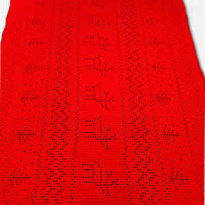 Puede incluir: Una vibrante manta roja tejida a crochet. La manta presenta un patrón repetitivo de caracteres estilizados y motivos florales. El diseño se crea mediante espacios abiertos en el tejido de crochet, creando un efecto texturizado. La manta se muestra sobre una superficie blanca.