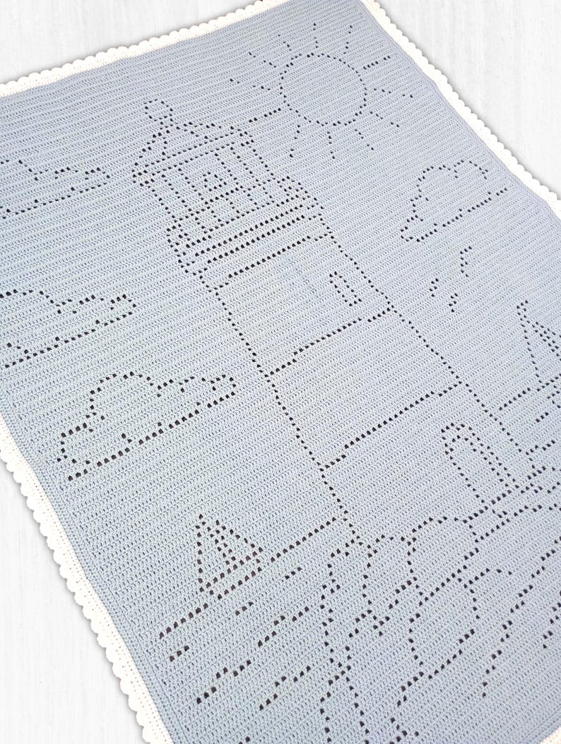May include: A light blue crochet blanket featuring a detailed lighthouse design created with openwork stitches. The pattern includes a sun, clouds, and a sailboat, finished with a delicate white scalloped border along the entire rectangular edge.