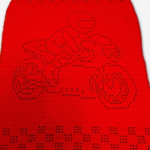 Puede incluir: Una manta roja brillante tejida a ganchillo con un diseño de puntos negros de una motocicleta y un piloto. La manta tiene un patrón de cuadros en el borde inferior y está hecha de hilo suave y texturizado.
