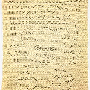 May include: A rectangular, pale yellow crochet blanket featuring a central design of a teddy bear with arms raised. Above the bear, the number 2022 is clearly visible, integrated into the stitch pattern. The entire piece is crafted with a consistent, uniform yarn texture throughout the design.