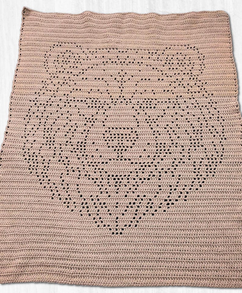 Pode incluir: Uma manta retangular de croch&ecirc; em uma cor rosa antigo s&oacute;lida. O tecido apresenta um design central de rosto de urso criado com uma t&eacute;cnica de croch&ecirc; fil&eacute;, onde espa&ccedil;os abertos no padr&atilde;o formam as orelhas, os olhos e o focinho do urso.