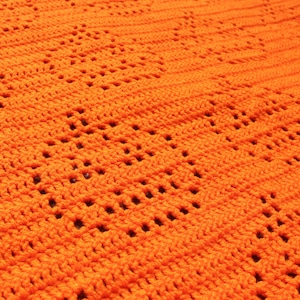 May include: Close-up of a handmade orange crochet blanket. The blanket features a repeating pattern of openwork squares, creating a textured surface. The bright orange color and intricate design suggest a cozy, handcrafted item, perfect for home decor.