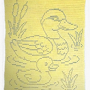 May include: A handmade, yellow crochet blanket featuring a duck design. The duck is outlined in black stitches, along with aquatic plants. The blanket is square-shaped and appears to be made of soft yarn.