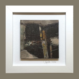 May include: Abstract painting in a white frame. The artwork features a dark, textured composition with shades of black, brown, and gold. Signed "Colette 2026" in the lower right corner. The painting is mounted on a white textured background.