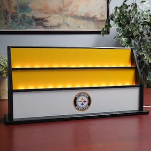 May include: A black, yellow, and white illuminated shelf unit. The unit features three yellow shelves with integrated lighting. The bottom section displays the Pittsburgh Steelers logo. The unit is designed to sit on a desk or table.