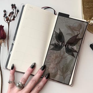 May include: An open planner with a weekly layout on the left page and a dark, semi-transparent vellum dashboard on the right. The dashboard features a black butterfly graphic, floral illustrations, and the name COURTNEY in white text.