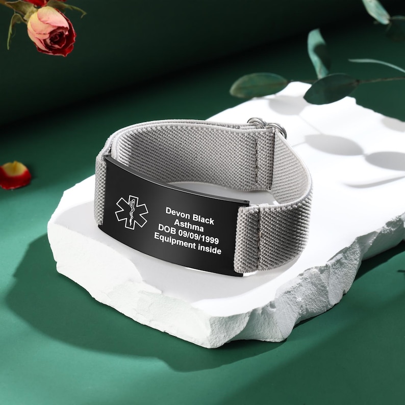 May include: A gray medical alert bracelet with a black plate. The plate has the medical symbol, the name "Devon Black", medical condition "Asthma", date of birth, and the text "Equipment inside".