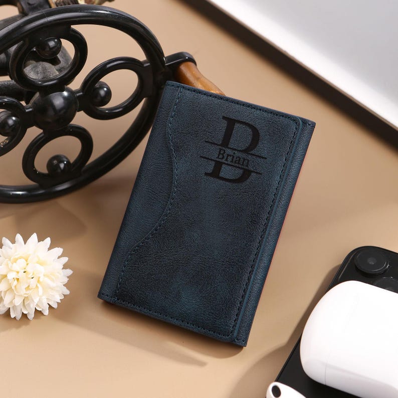 May include: A dark blue leather wallet with a personalized monogram of the letter "B" and the name "Brian" engraved on the front.