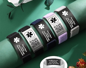 Op de afbeelding: Vijf verschillende medische armbandjes met zwarte en witte tekst. De armbandjes zijn gemaakt van een rekbaar materiaal en hebben een metalen plaatje met een ster-van-leven-symbool en een QR-code. De tekst op de armbandjes luidt "Devon Black, Astma, Geb. 09/09/1999, Uitrusting binnenin". De armbandjes liggen op een groene achtergrond.