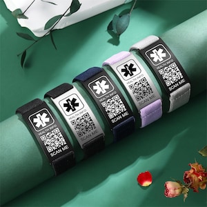 May include: A collection of medical alert bracelets in various colors, including black, navy, lavender, and gray. Each bracelet features a metal plate with a medical symbol, "HEALTH INFO," and a QR code that says "SCAN ME."