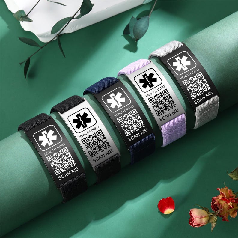May include: A collection of medical alert bracelets in various colors, including black, navy, lavender, and gray. Each bracelet features a metal plate with a medical symbol, "HEALTH INFO," and a QR code that says "SCAN ME."