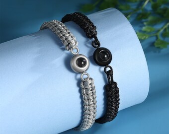 Könnte beinhalten: Zwei geflochtene Armbänder mit einer silbernen und schwarzen Perle. Die Perlen haben eine kleine, runde, reflektierende Oberfläche.