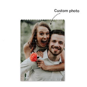 Peut inclure: Un couple sourit et rit en posant pour une photo. La femme porte une robe blanche et tient une fleur rose. L'homme porte une chemise blanche et a son bras autour de la taille de la femme.