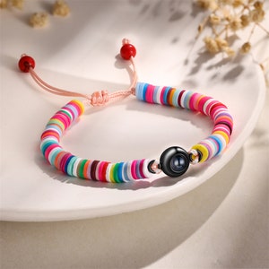 Op de afbeelding: Een kleurrijke armband met een zwarte kralenbedel. De armband is gemaakt van kleine, ronde, kleurrijke kralen en heeft een koordsluiting.
