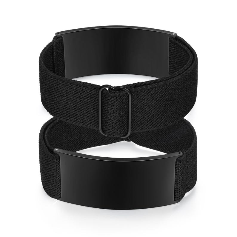 May include: Two black elastic shirt stays with rectangular metal plates. The stays are designed to keep shirts tucked in and are made of a woven fabric. The metal plates are a solid black color.