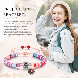 Op de afbeelding: Een kleurrijke kralen armband met een projectiesteen. De armband is roze en heeft een verscheidenheid aan gekleurde kralen. De projectiesteen is zilverkleurig en heeft een klein beeldje erin. De armband ligt op een witte achtergrond.