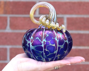 May include: A glass pumpkin with a swirling gold stem. The pumpkin is iridescent blue and purple with a marbled pattern.
